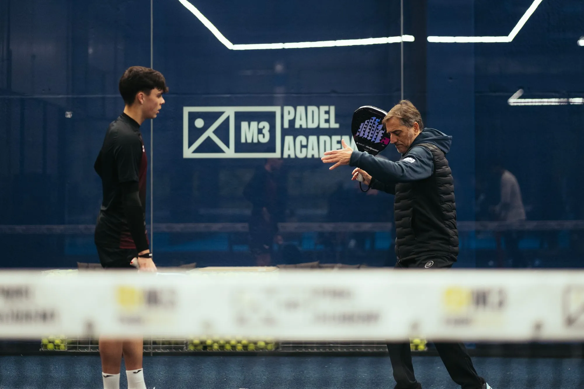 M3 coach demonstrating a padel stroke to a player on court