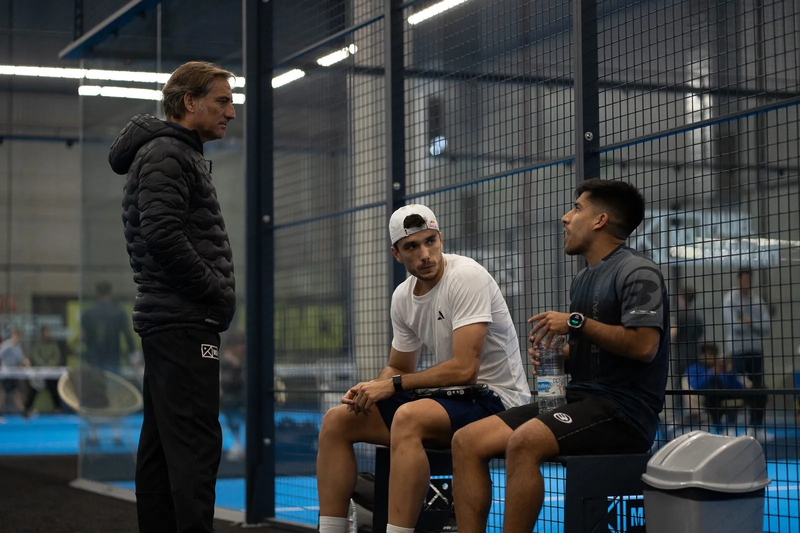 M3 coach coaching two padel players courtside at The District