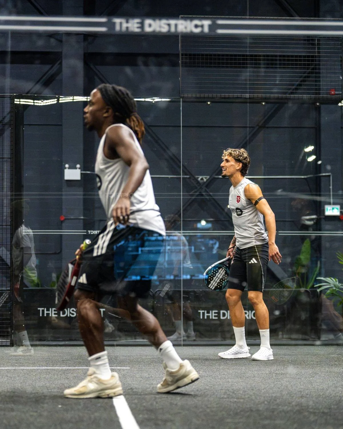 Two Toronto FC players rally on a glass padel court at The District